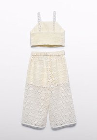 Set di due pezzi all'uncinetto in un caldo crema. Presenta un top corto con spalline sottili e pantaloni corti a gamba larga con un motivo in pizzo ricamato.