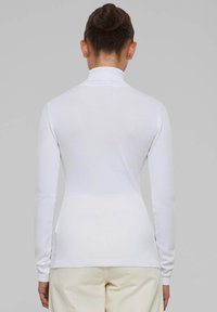 Top bianco a maniche lunghe con colletto alto, texture a maglia, design aderente e polsi a costine, che mostrano linee morbide e pulite.