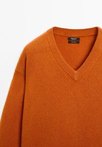 Orangenes V-Ausschnitt-Pullover aus 100 % Kaschmir, mit einem gerippten Ausschnitt und weicher Textur. Pflegeetikett im Nacken sichtbar.