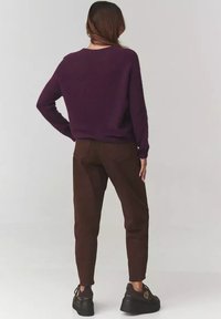 Fioletowy dzianinowy sweter o luźnym kroju, w połączeniu z ciemnobrązowymi spodniami. Czarne buty na platformie dopełniają całość. Faktura wydaje się miękka.