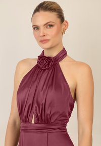 Burgunderfarbenes Halfterkleid aus Satin mit einem Rosenakzent am Ausschnitt, ausgestattet mit gefältelten Details und einem Ausschnitt in Form eines Schlüssellochs.