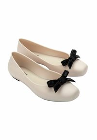 Zapatos planos de color rosa claro fabricados con goma suave, con punteras redondeadas y un lazo negro como acento en cada zapato.
