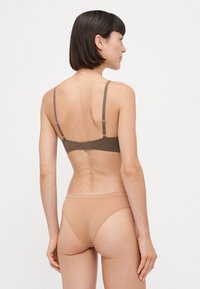 Bruine bh met verstelbare bandjes; glad, rekbaar materiaal. Gecombineerd met naadloze huidkleurige slip, beide met eenvoudige, minimalistische ontwerpen.