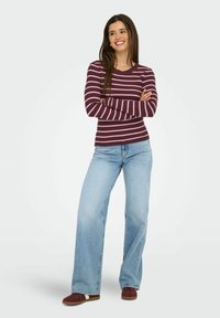 Haut à manches longues en côte rayé bordeaux et rose, associé à un jean taille haute large bleu clair et des baskets marron. Texture en coton lisse.