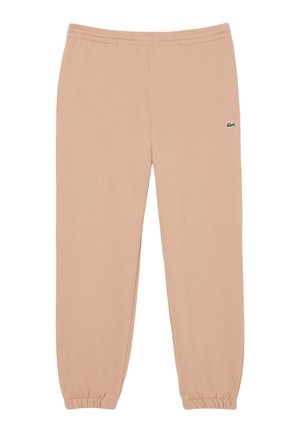Różowe spodnie dresowe w kolorze brzoskwiniowym, z elastycznymi mankietami i pasem, z małym zielonym logo Lacoste na lewym udzie. Miękka tekstura materiału.