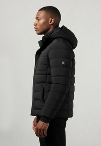 Juodas pūkuotas džemperis su kapišonu, turintis siuvinėtus skyrius, užtrauktukų kišenes ir guminius rankogalius. Lygus paviršius su elegantiška siluetu.