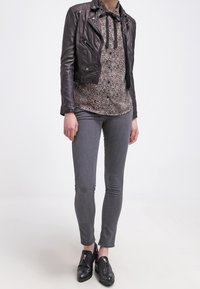 Sort læder cropped jakke, leopardtrykt skjorte med sløjfe, grå tætsiddende jeans og sorte slip-on sko med guldfarvede detaljer.