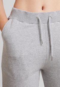 Grå sweatpants med ribbat midjeband, dragsko och sidofickor; tillverkade av mjukt, texturerat tyg.