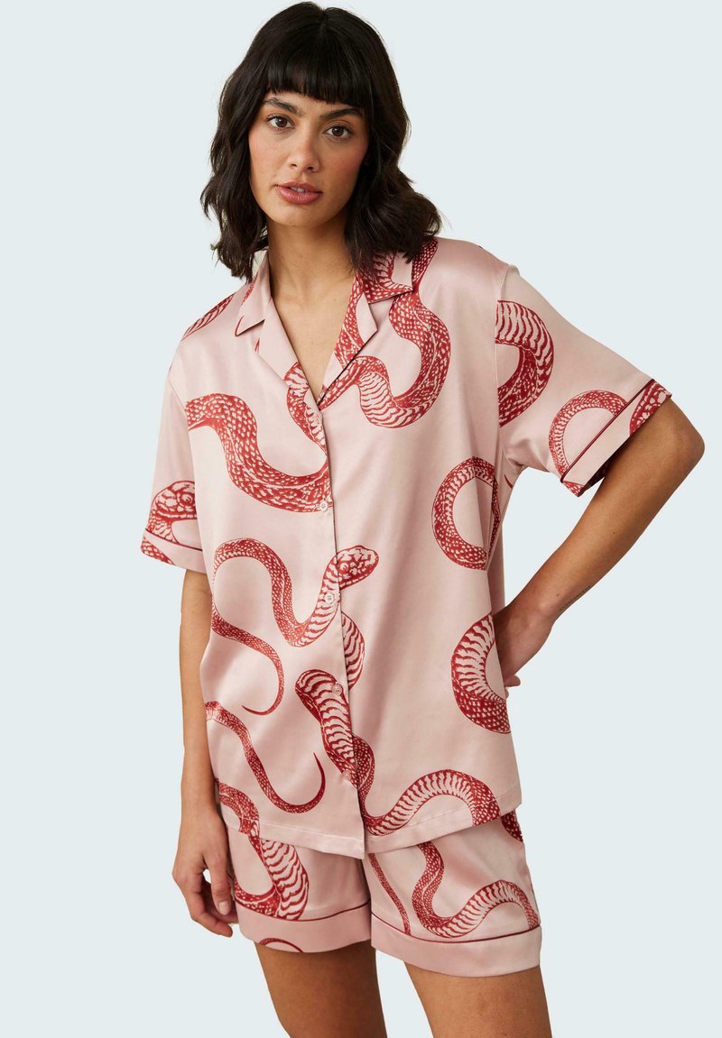 Short-sleeve pink pajama set with a snake pattern in red. Satin fabric, relaxed fit, featuring discreet buttons and contrasting trim.