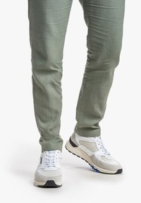 Scarpe da tennis bianche con dettagli grigi, tomaia in mesh testurizzato, suola nera e blu, abbinate a pantaloni tapered verde chiaro.