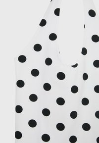 Haut blanc sans manches avec un col rond présentant un motif à pois noirs réparti uniformément sur le tissu.