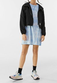 Czarna krótka kurtka z elastycznymi mankietami, w połączeniu z jasnoniebieską sukienką tie-dye. Obuwie to sneakersy w kolorach blokowych z masywną podeszwą.