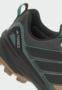 Czarne buty sportowe z teksturowaną siateczką i zielonymi akcentami, gumową podeszwą oraz wyraźnym logo z boku.