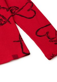 Červená žebrovaná halenka s dlouhým rukávem s černými srdíčky a křížovými vzory. Obsahuje malou červenou etiketu se symbolem na lemu.