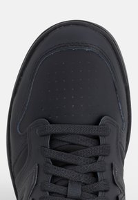 Gros plan sur la partie avant d'une basket en cuir noir avec des lacets noirs et de petites perforations sur la zone des orteils.