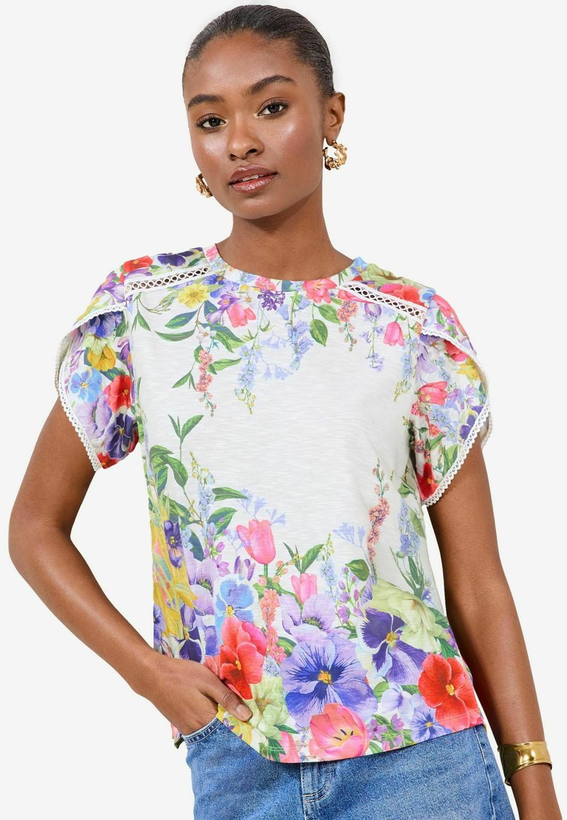 Maglietta a maniche corte floreale caratterizzata da un mix di fiori colorati su uno sfondo chiaro, con dettagli in pizzo sulle spalle e una vestibilità comoda.
