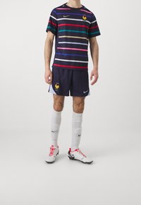 Marinblå och flerfärgad randig Nike fotbollströja, matchande shorts, vita strumpor och rödprickiga fotbollsskor med svarta detaljer.