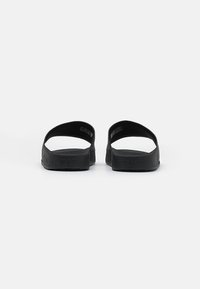 Sandalias negras con una suela texturizada y una correa superior ancha, con un diseño minimalista. No hay adornos ni patrones visibles.