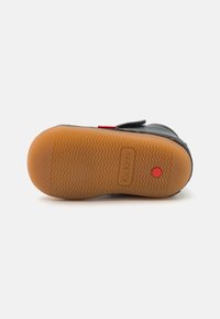 Černá kožená bota s texturovanou gumovou podrážkou, která má červený akcent a suchý zip. Podrážka má cik-cak vzor pro lepší grip.