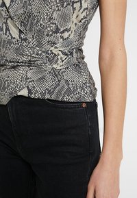 Topp avskuren med ett beige och svart ormskinnstryck, med en vriden framdesign. Ihop med högmidjade svarta denimjeans.