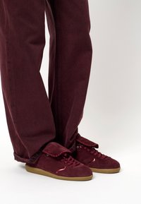 Bordeauxsuède sneakers met een klep en een contrasterende gumzool, gecombineerd met bordeaux gestructureerde broeken in een relaxed fit.