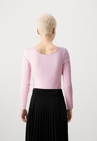 Lys pink langærmet bluse med rund halsudskæring, parret med en sort plisseret nederdel med bred talje og glat tekstur.