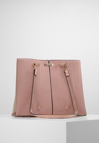 Sac à main en cuir rose doux avec ferrures dorées, double poignée, et silhouette rectangulaire reposant sur un socle blanc contre un fond gris uni.