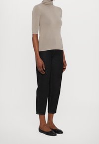 Jersey de cuello vuelto beige, ajustado, con mangas tres cuartos; combinado con vaqueros oscuros recortados y bailarinas negras. Textura de tela suave.