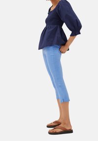 Persona con una blusa azul marino con volantes y mangas abullonadas, jeans cortos de mezclilla azul claro con pequeñas aberturas en los lados, y chanclas de plataforma marrones.