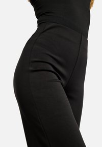 Mustad vormivad püksid, mis on valmistatud siledast kangast, kõrge vöökohaga ja ilma nähtavate õmblusteta, rõhutades detailset lõiget.