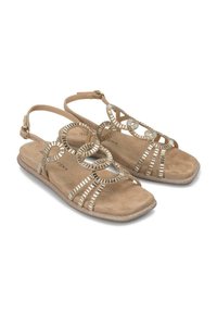 Sandales en daim beige avec des accents métalliques, dotées de découpes circulaires et de semelles plates. Sangle de cheville ajustable pour un maintien sécurisé. Design à bout carré.
