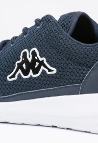 Marinblå mesh-sneaker med vita accenter, prydd med en Kappa-logotyp i form av två sittande figurer. Strukturerad ovandel och gummisula.