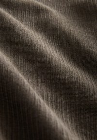 Nahaufnahme von beiger gerippter Strickware mit sanften Falten und sichtbar vertikaler Nahttextur.