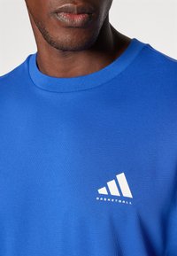 Blue cotton t-shirt featuring a white Adidas logo and "BASKETBALL" text. The design includes a round neck and short sleeves.