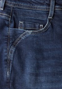 Tummansininen farkkujen materiaali, jossa etutasku ja kontrastiväriset saumat. Kangas on sileä ja siinä on kevyt kiilto.