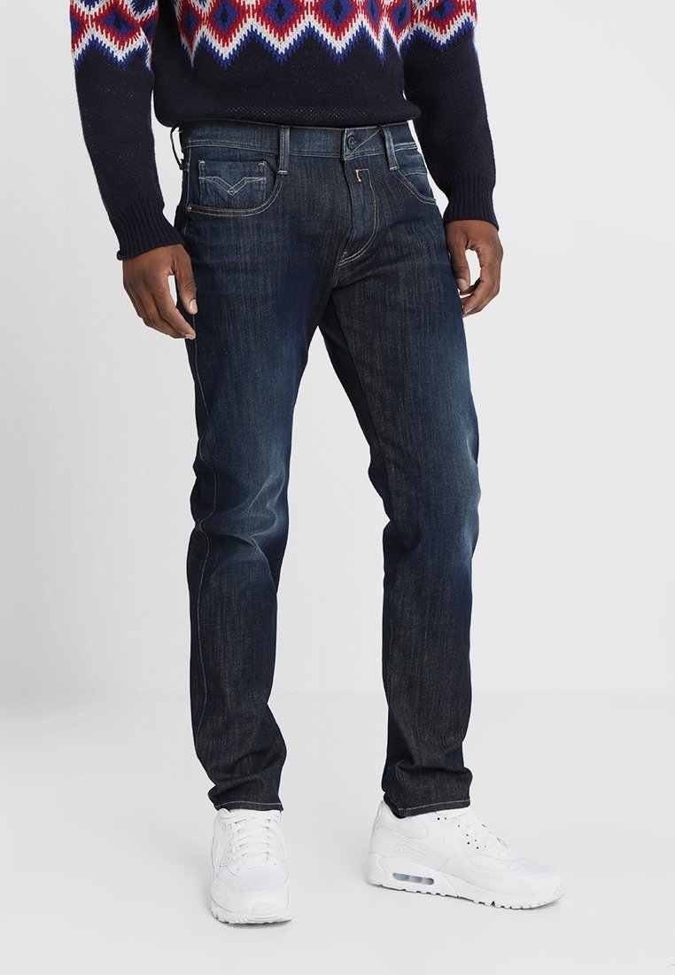 Mörkblå denimjeans med slim fit, fem fickor och synlig sömnad. Bärs med en mönstrad tröja och vita sneakers.