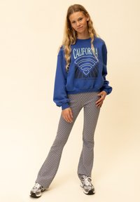 Blauwe trui met de opdruk "CALIFORNIA" en wijde broek met patroon in tinten blauw en wit, gecombineerd met grijze sneakers.