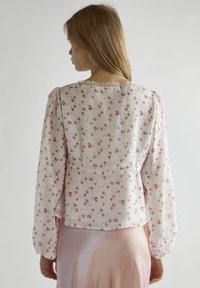 Blusa a fantasia floreale in tessuto leggero, con maniche lunghe a sbuffo, delicata bordatura in pizzo sullo scollo e un taglio leggermente accorciato.