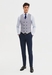 Szary, dwurzędowy kamizelka nałożona na jasnoniebieską koszulę, zestawiona z ciemnoniebieskimi spodniami i czarnymi butami. Gładka tekstura, dopasowany krój i schludny design.