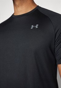 Camiseta atlética negra de manga corta con escote redondo. Fabricada en tela suave con un logo gris en la parte superior izquierda del pecho.