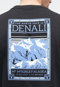 Μαύρο βαμβακερό T-shirt με γραφικό εκτύπωσης μπλε βουνών, κείμενο «The North Face of Denali» και διακοσμητικές λεπτομέρειες περιγράμματος.
