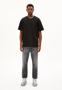 Black cotton t-shirt with a round neckline, paired with faded grey jeans and gray sneakers. Displayed on a neutral background.