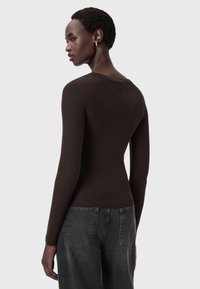 Bruine geribbelde top met lange mouwen en een ronde hals, nauwsluitende pasvorm en textielstructuur, gecombineerd met high-waisted donkere jeans.