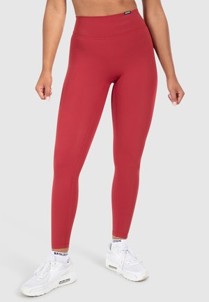 Red high-waisted leggings made of stretchy material. Smooth texture with flat seams. Paired with white athletic shoes.