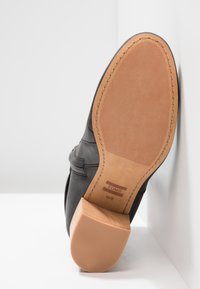 Chaussure en cuir noir à bout rond, dotée d'une semelle en caoutchouc marron clair et d'un talon empilé. Présente une texture de surface et des accents cousus.
