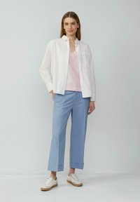 Witte button-up shirt over een lichtroze v-hals top, gecombineerd met lichtblauwe cropped broek en witte sneakers met beige accenten.