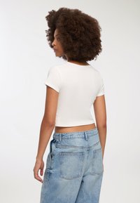Biała, krótka koszulka z krótkim rękawem, zestawiona z jasnoniebieskimi dżinsami o wysokim stanie, posiadającymi klasyczny pięciozakresowy krój.