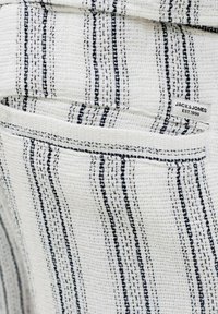 Tissu blanc texturé avec des rayures verticales noires, montrant une poche et une étiquette de marque Jack & Jones cousue près du bord.