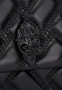 Borsa a tracolla in pelle trapuntata nera con un particolare clasp metallico nero a forma di mano, arricchito da dettagli in gioiello. Texture liscia e finitura lucida.