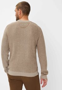 Light brown knitted sweater with a textured pattern and ribbed cuffs. Features a crew neck and slightly fitted silhouette.